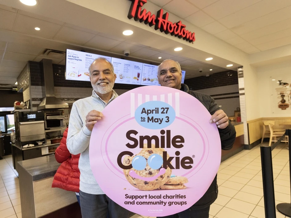 Barh Dhahan and Gurtek Shoker hold a "Smile Cookie" sign at a Tim Hortons location in Surrey.
